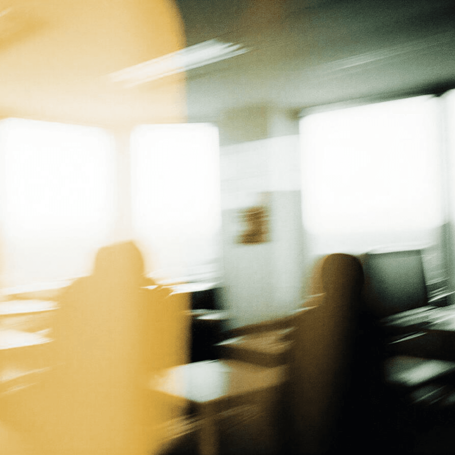 Blurry image of a room with light streaming through large windows, casting shadows and creating an abstract, motion-filled scene.
