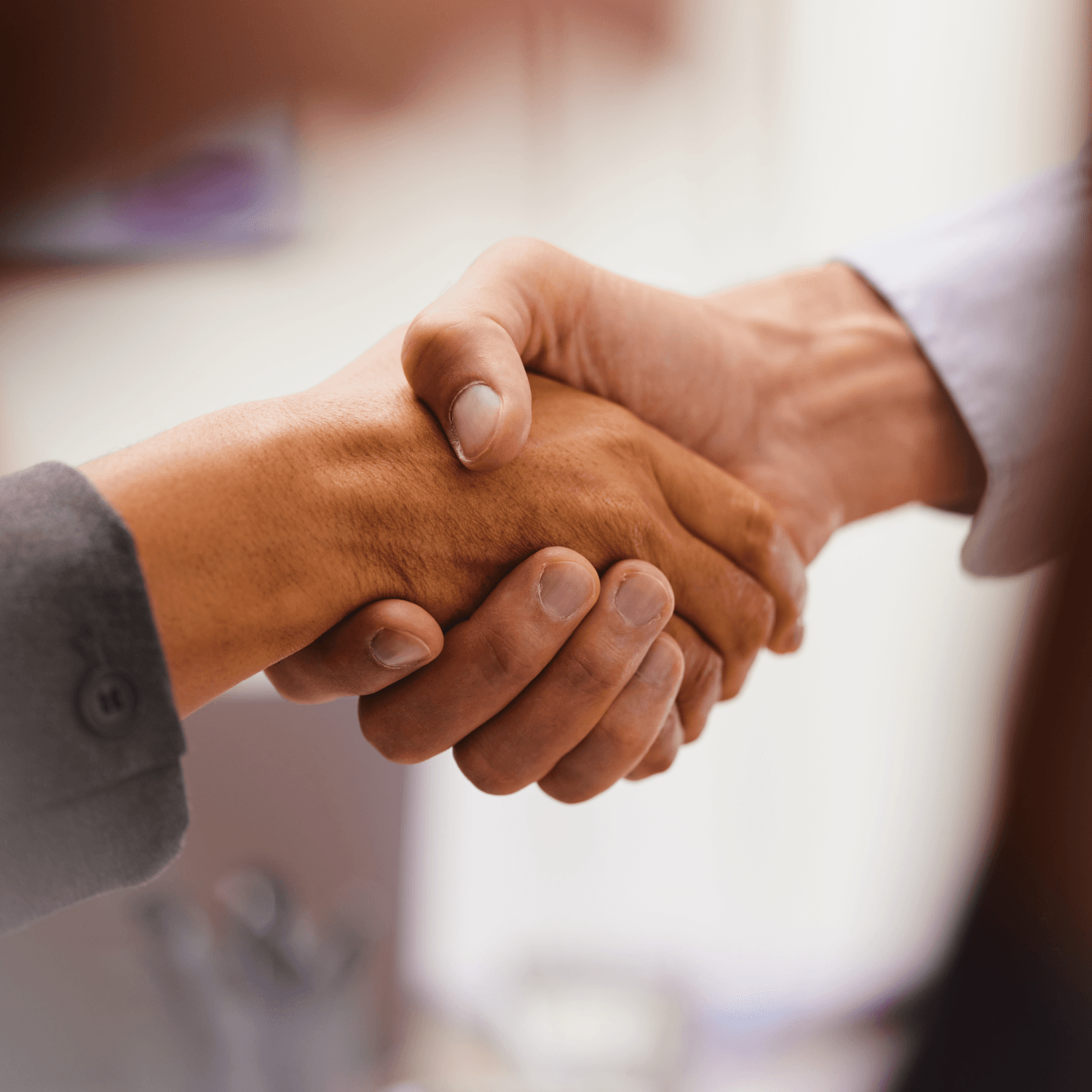 Two people shaking hands, one wearing a suit jacket and the other a shirt, symbolizing agreement or greeting.
