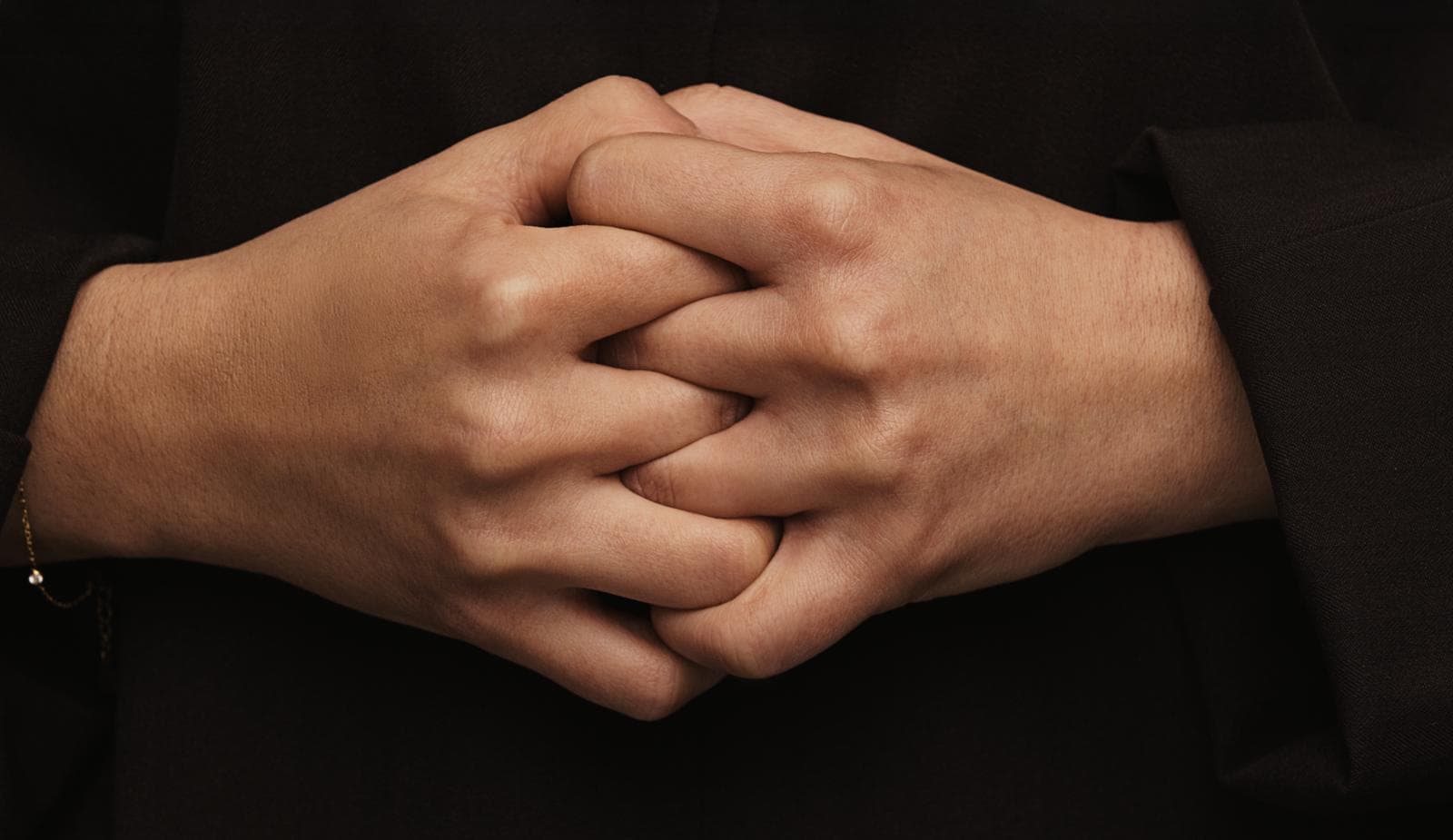Two hands clasped together against a dark background, expressing a sense of calm or contemplation.