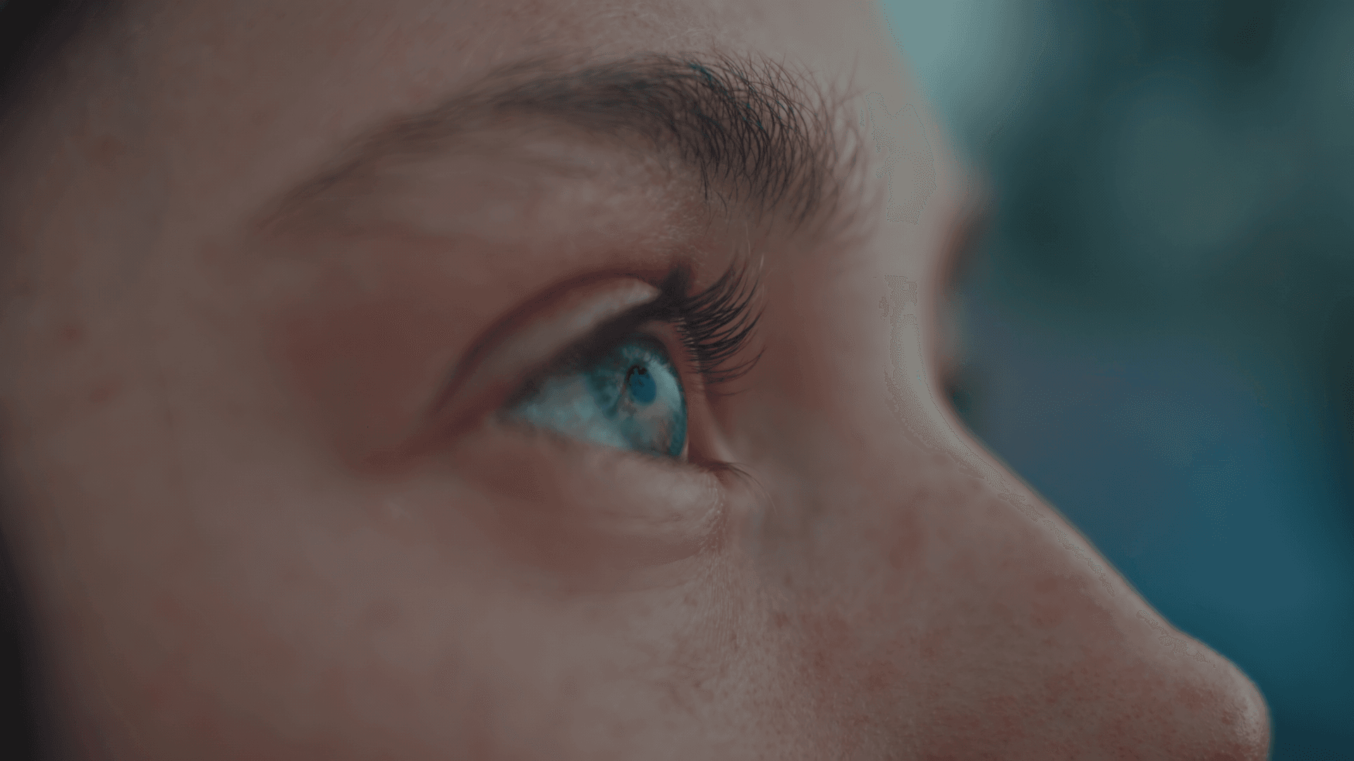 Close-up of a person's blue eye looking upwards, with clear lashes and freckles visible on the skin.