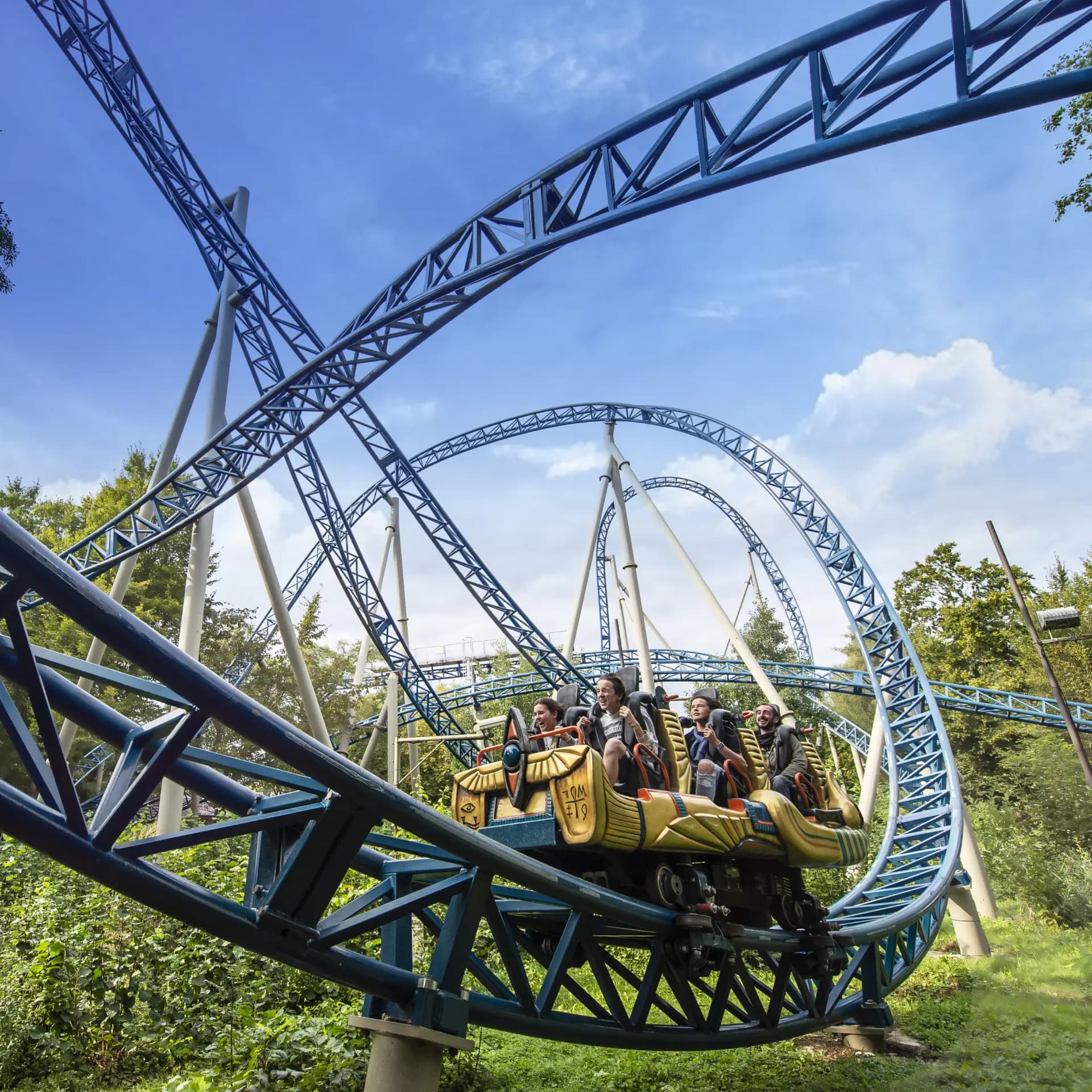 People riding a blue roller coaster with loops and twists against a clear blue sky.