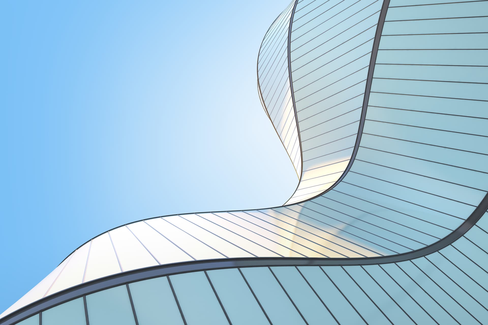 Modern glass building with curved, wavy panels reflecting light against a clear blue sky.