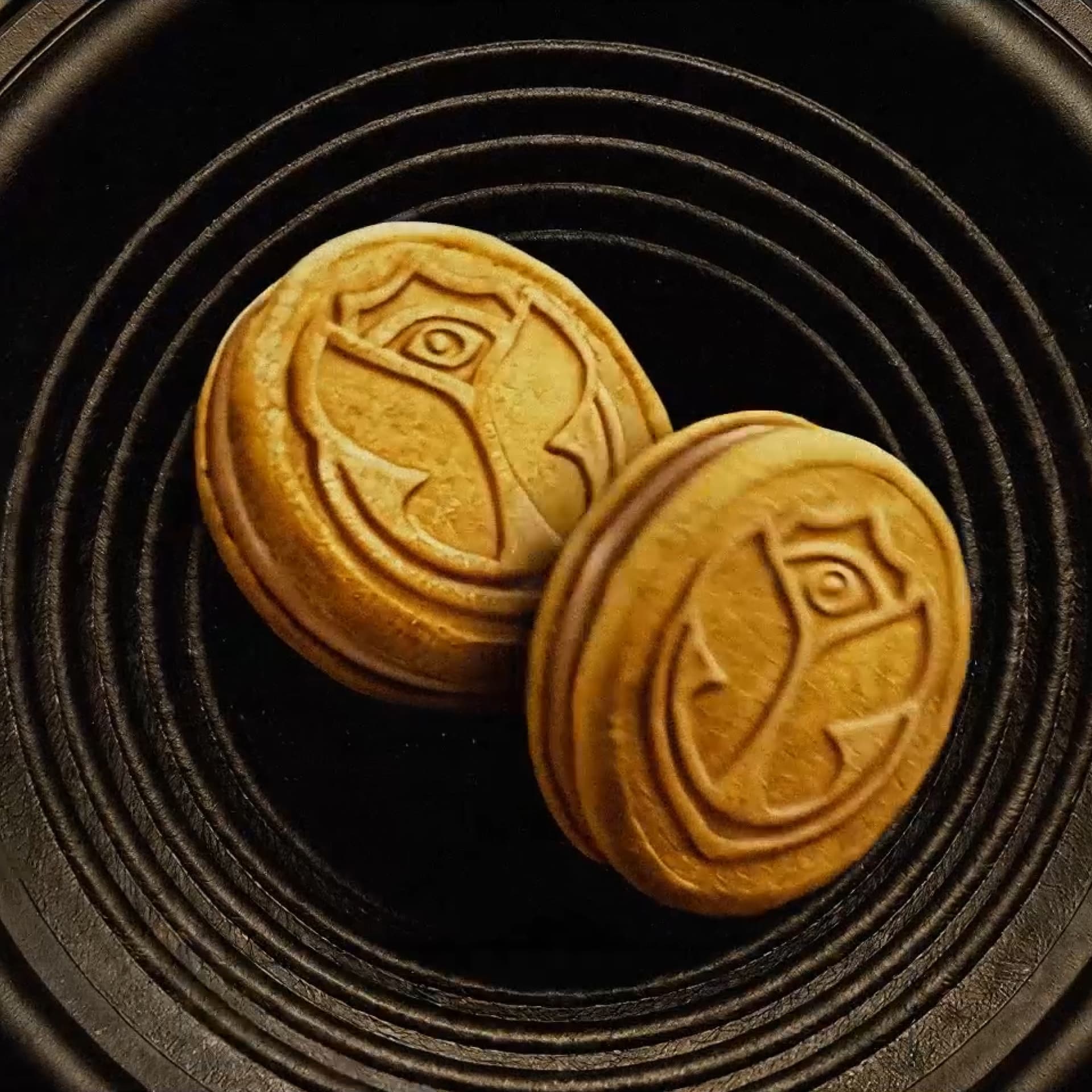Two round mooncakes with intricate designs on top, placed on a textured black plate.