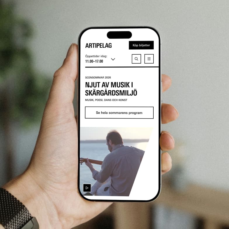A hand holding a smartphone displaying an event page for a music festival, featuring a guitarist by the sea with the text in Swedish.